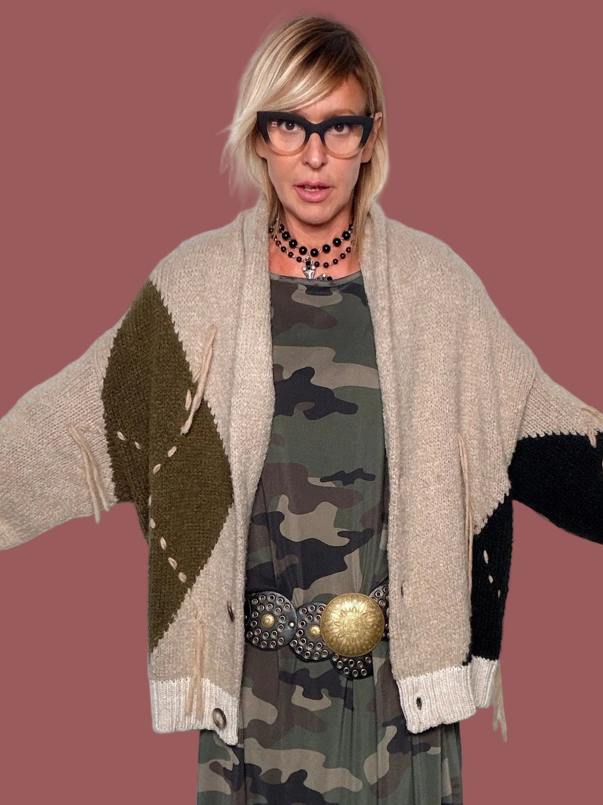 Cardigan beige con rombo militare sul davanti, dettagli neri sulle maniche e frangie, portato aperto, vista frontale con braccia aperte