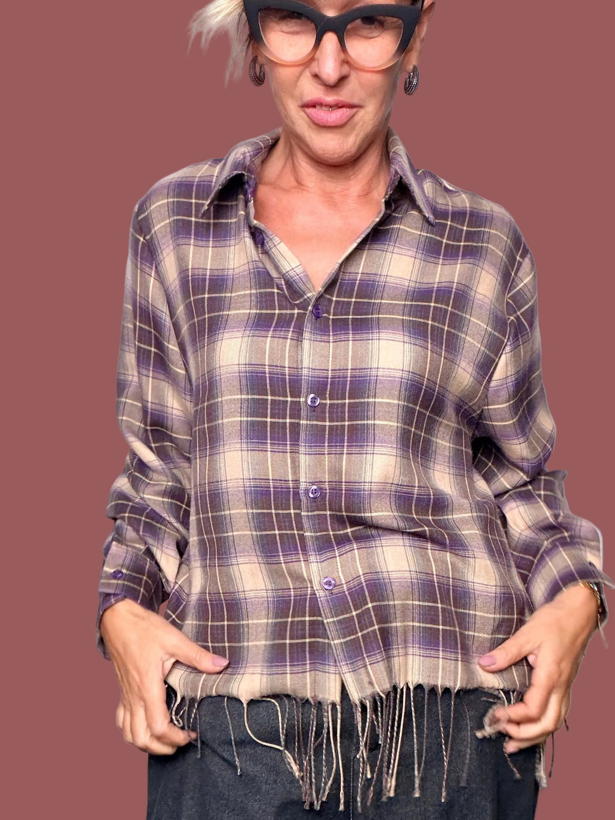 Dettaglio della camicia a quadri beige e viola con bottoni e frange decorative al fondo