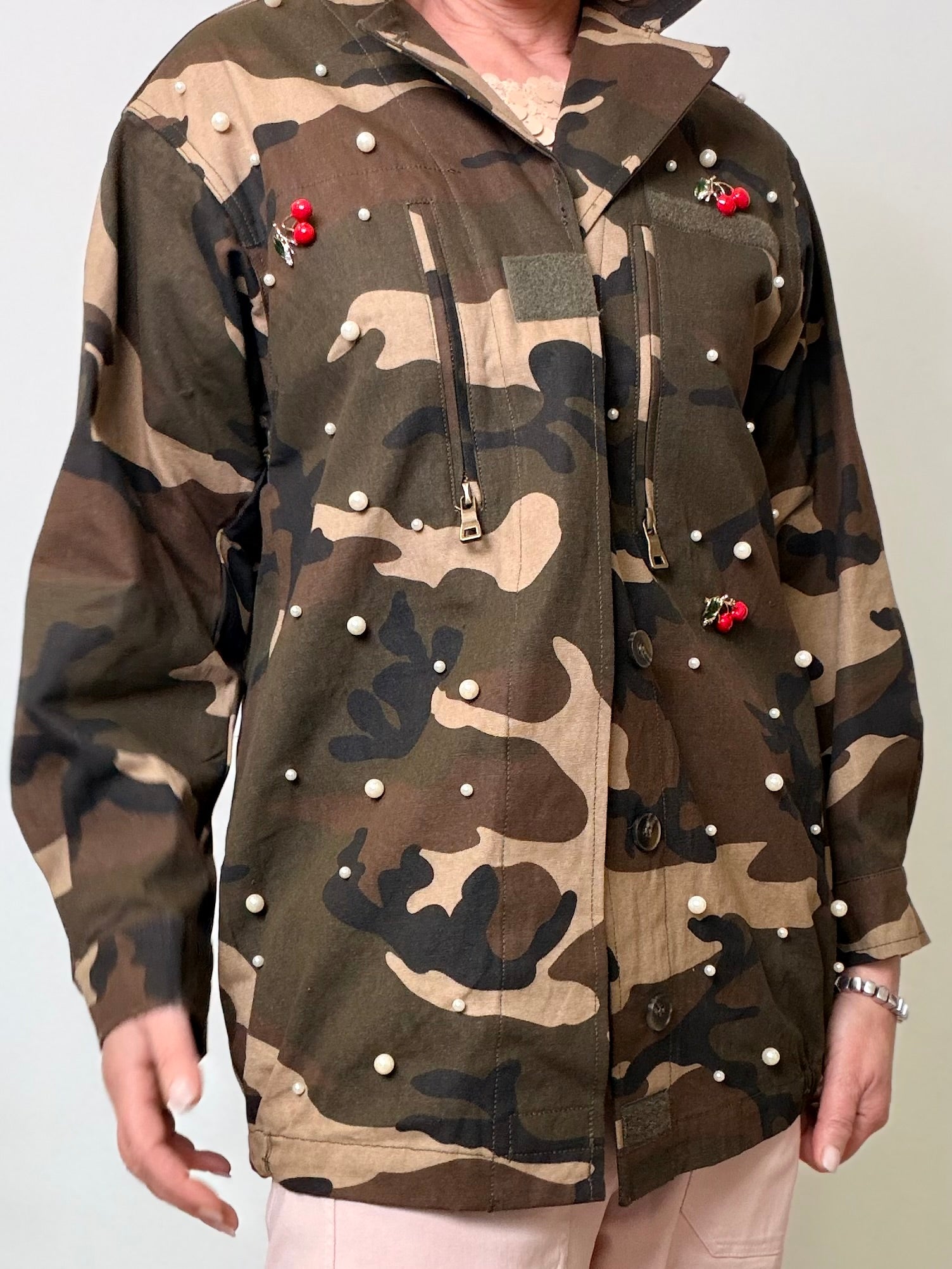 Giacca oversize camouflage verde militare con perle applicate e spille ciliegie rosse.
