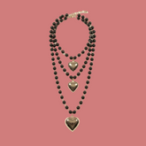 Collana multistrato nera con tre pendenti a cuore su fondo neutro