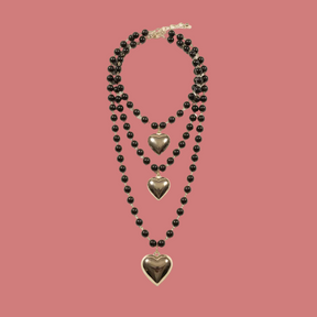 Collana multistrato nera con tre pendenti a cuore su fondo neutro